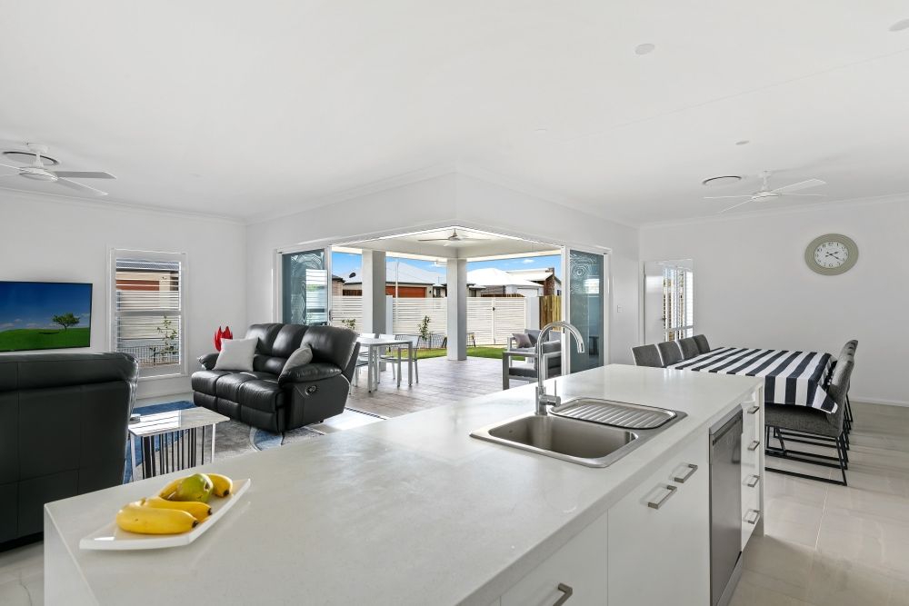 A kitchen and living room in a house with a clock on the wall. — Peter Betros Homes in Highfields, QLD