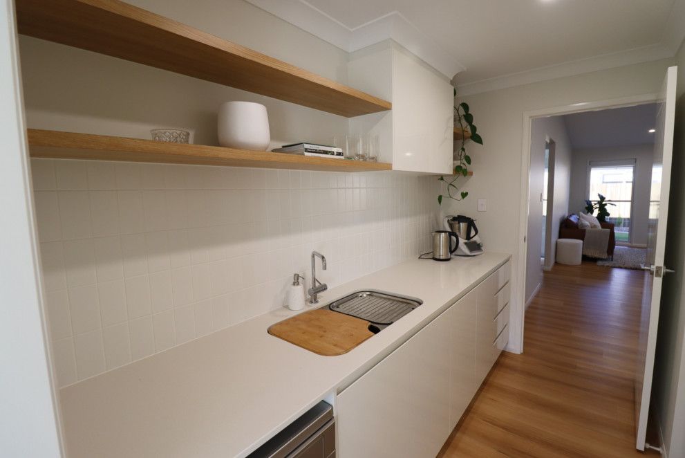A kitchen with a sink , dishwasher , and wooden shelves. — Peter Betros Homes in Highfields, QLD