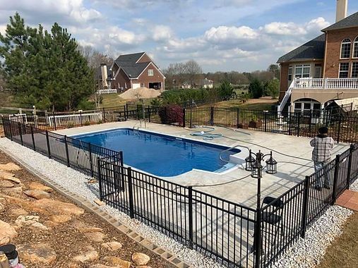 A large swimming pool surrounded by a fence and a brick house.