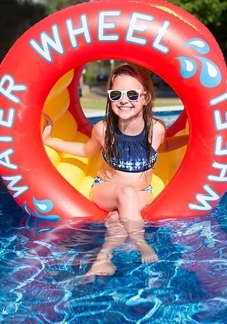 A young girl is sitting inside of an inflatable wheel in a swimming pool.