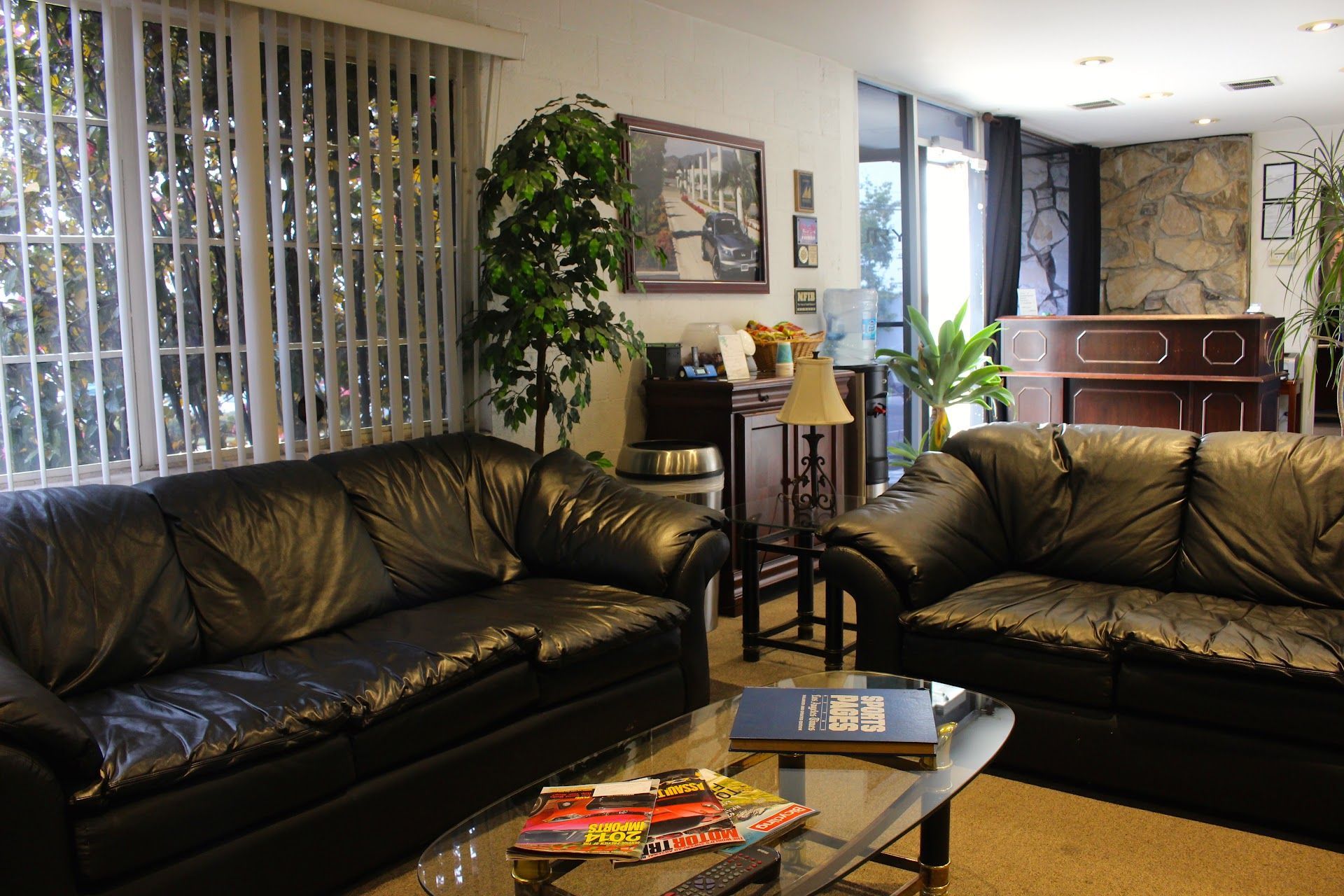 Living room with two black leather sofas, glass coffee table, piano, and vertical blinds | Luxury Motorworks