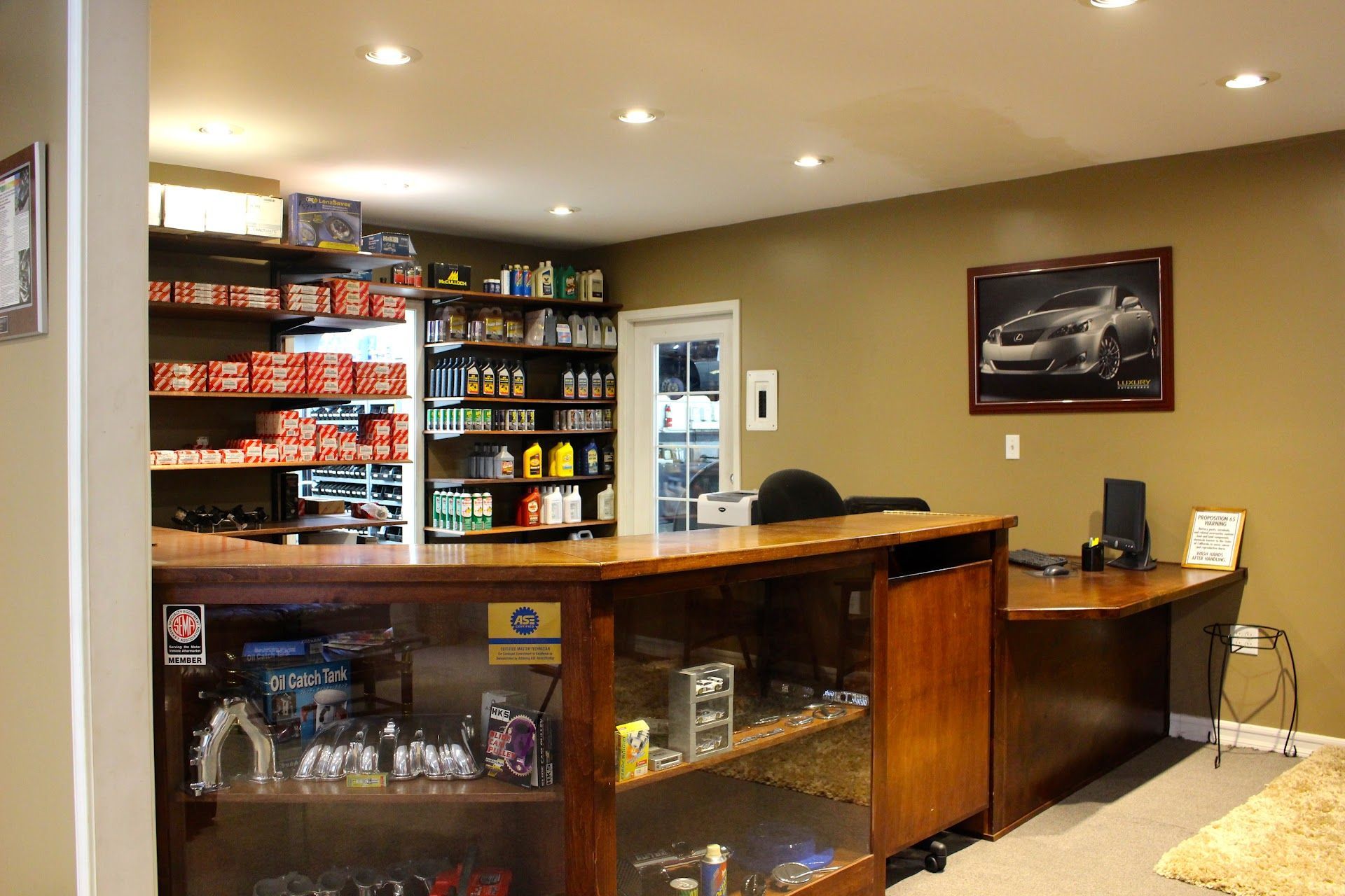 Small bar with shelves of snacks and drinks, wooden counter, and a desk in a warmly lit room. | Luxury Motorworks