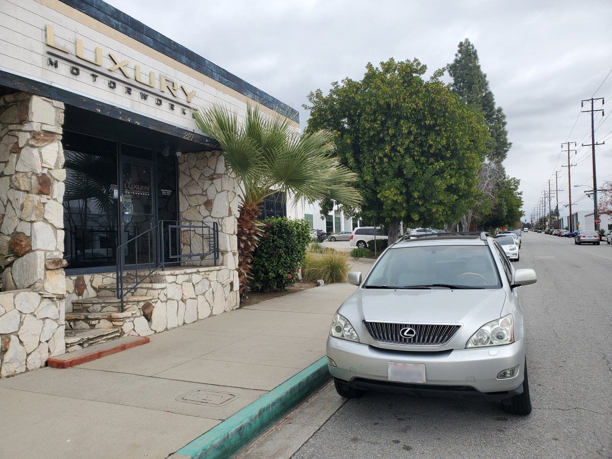 Silver SUV parked along a sidewalk beside a stone building on a city street | Luxury Motorworks