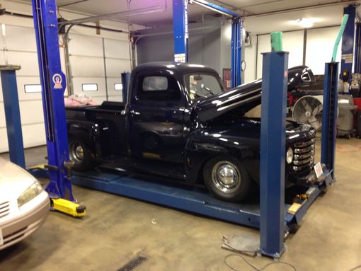 Black vintage pickup truck on a car lift in an auto repair shop with hood open