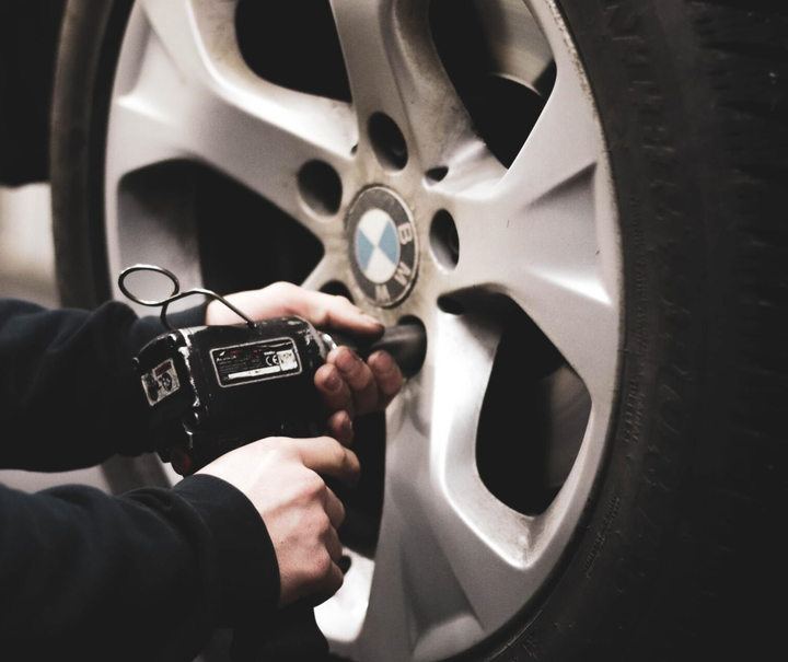 Hands using a power tool on a BMW wheel hub to remove a lug nut.