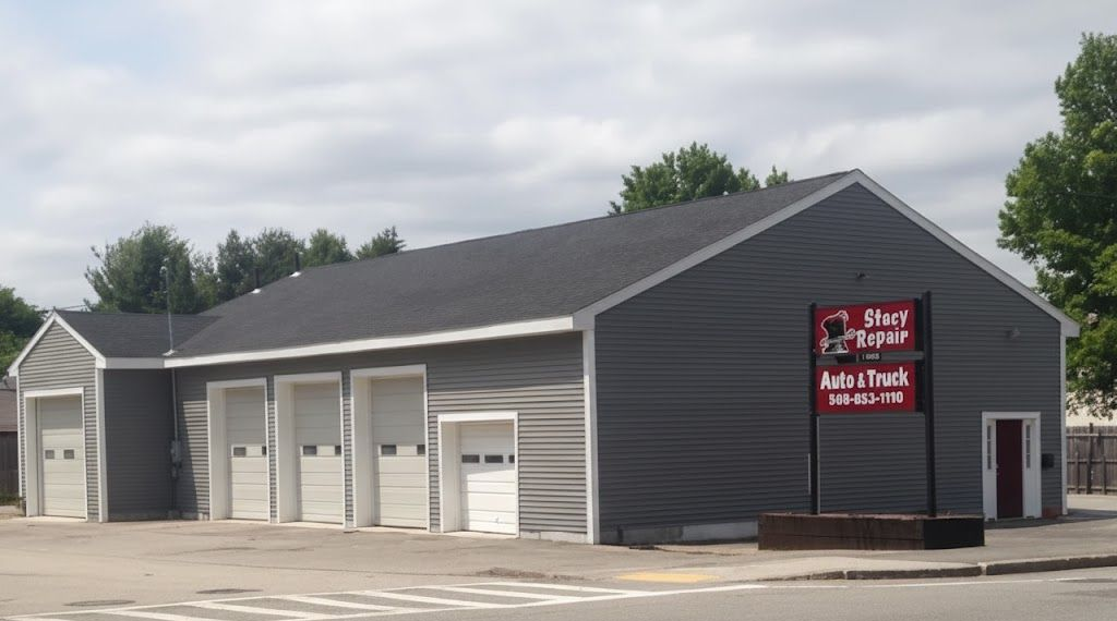 Dark gray auto repair building with several white garage doors and a red sign near the entrance