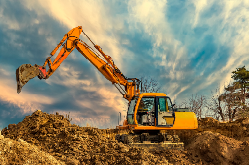 Orange excavator digging a dirt mound under a cloudy sky at sunset