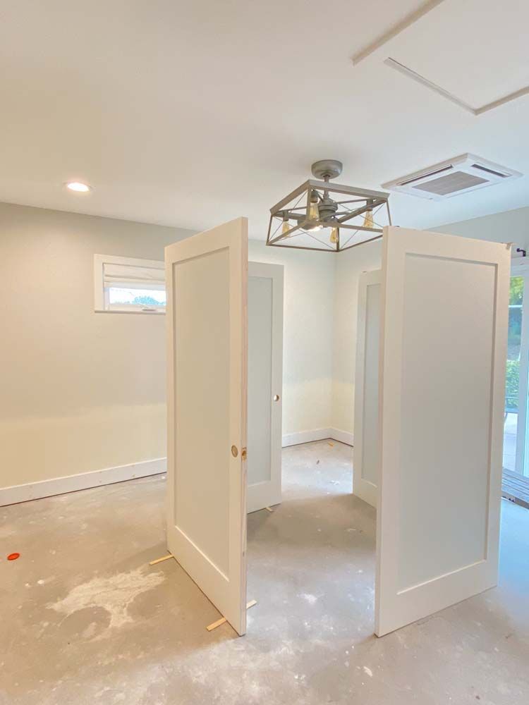 Three white doors open to reveal an empty room, unfinished construction with a ceiling light.
