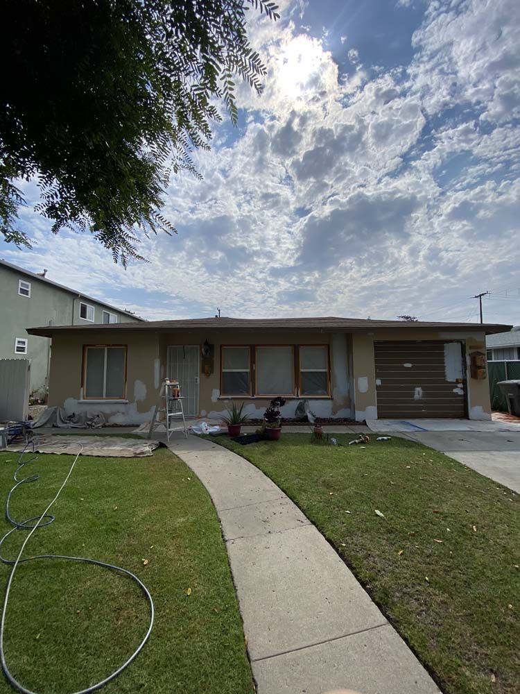 House exterior undergoing renovation, cloudy sky, concrete pathway leading to front door, brown garage door.