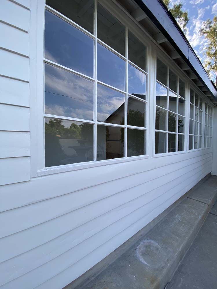 White house exterior with large grid windows reflecting sky and surroundings.