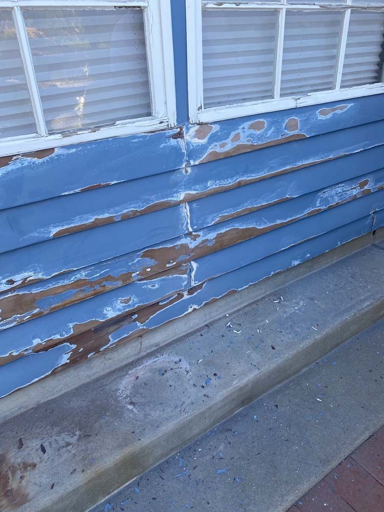 Blue siding with peeling paint below a window and concrete steps.