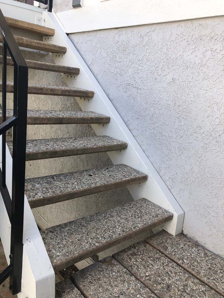 Outdoor staircase with speckled treads, white risers, and a black handrail.