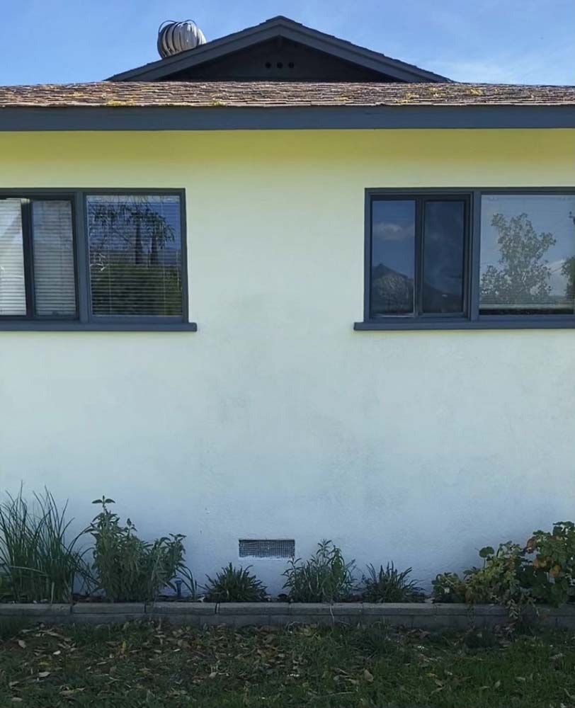 Light yellow house with dark gray windows and roof trim. Low bushes in front.