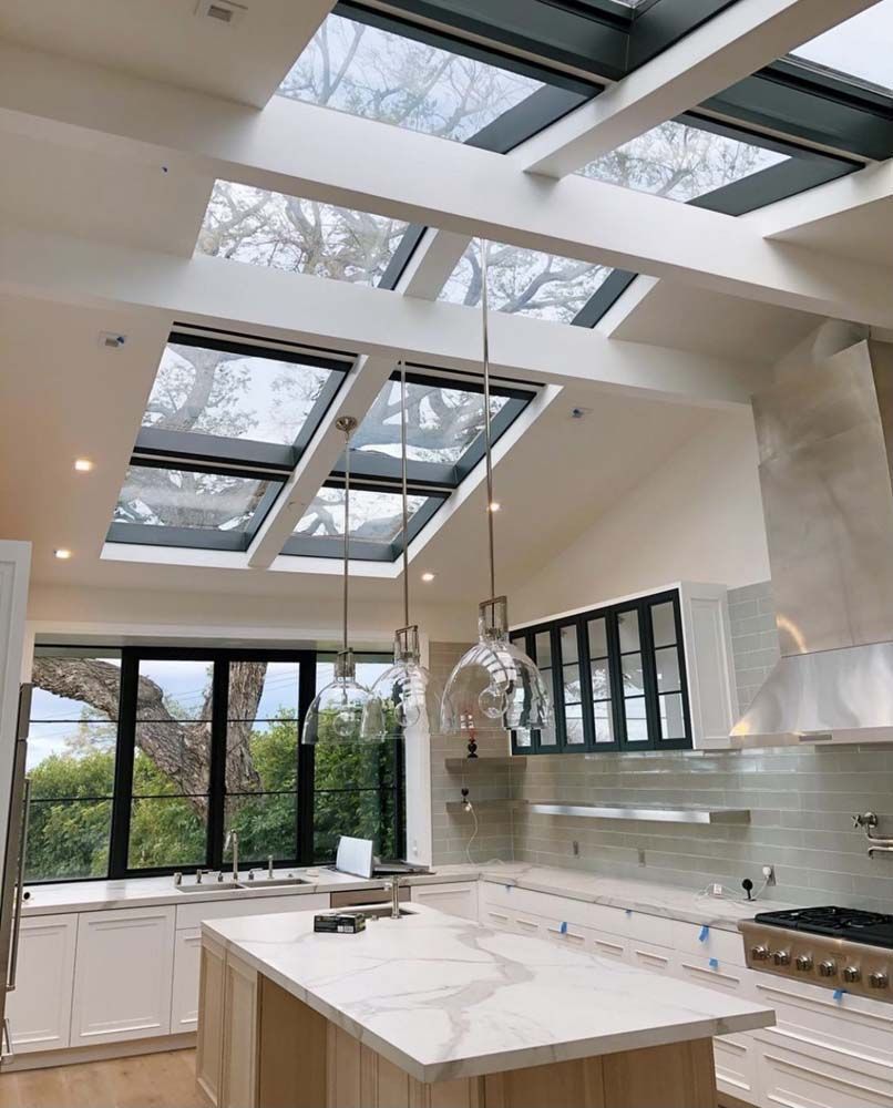 Kitchen with skylights, island, and large windows overlooking trees.
