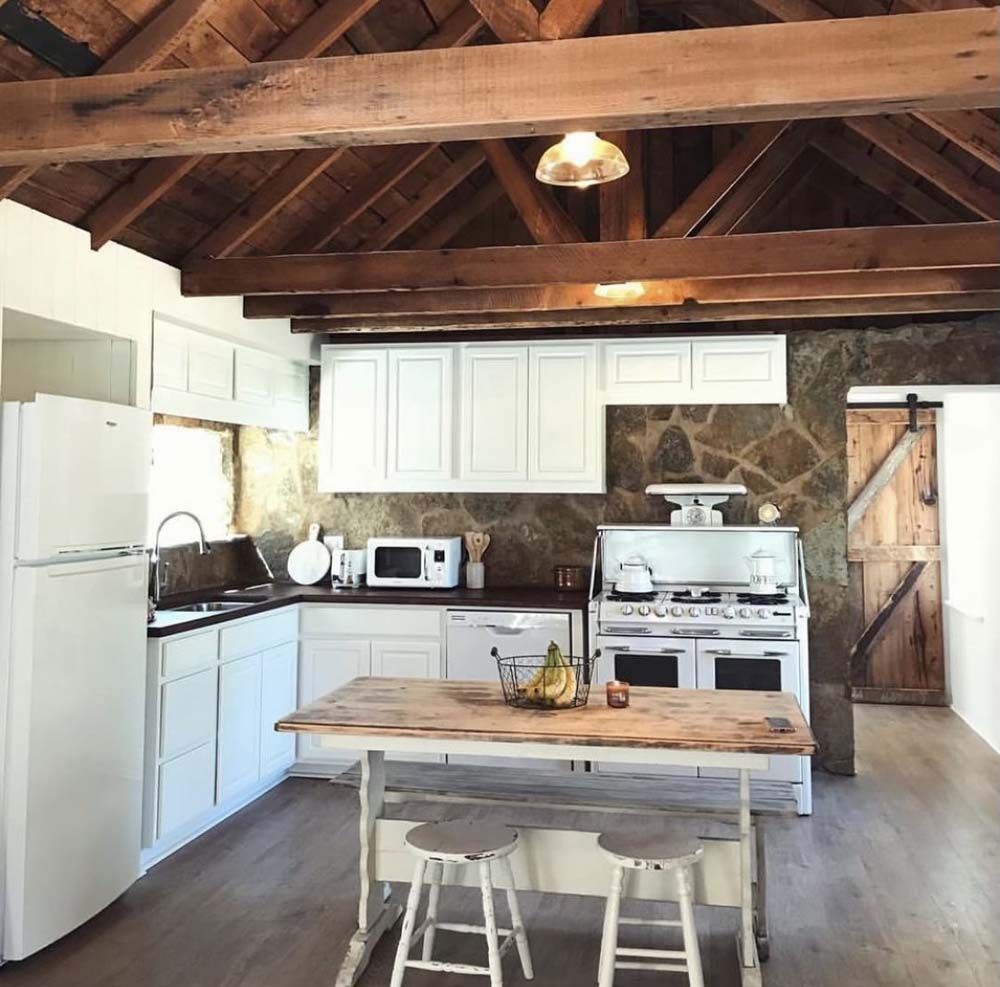 Rustic kitchen with white cabinets, wood ceiling, stone wall, and a wood island with stools.