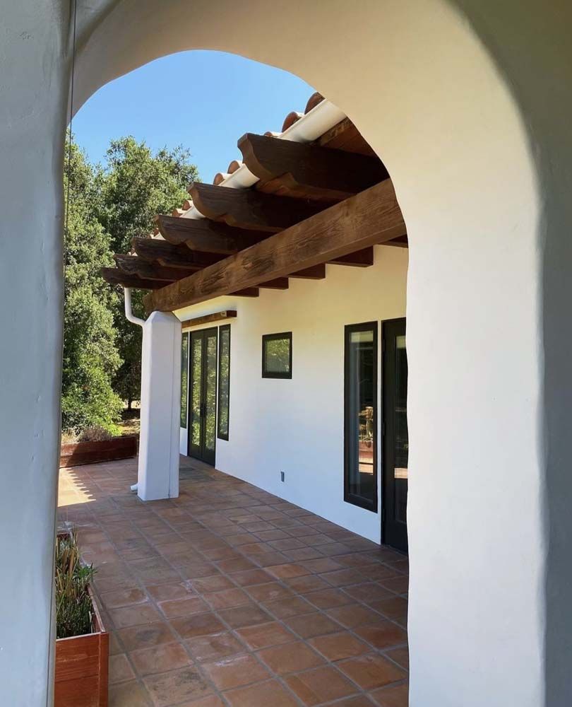Terracotta-tiled patio framed by an archway, leading to a white stucco building with dark trim.