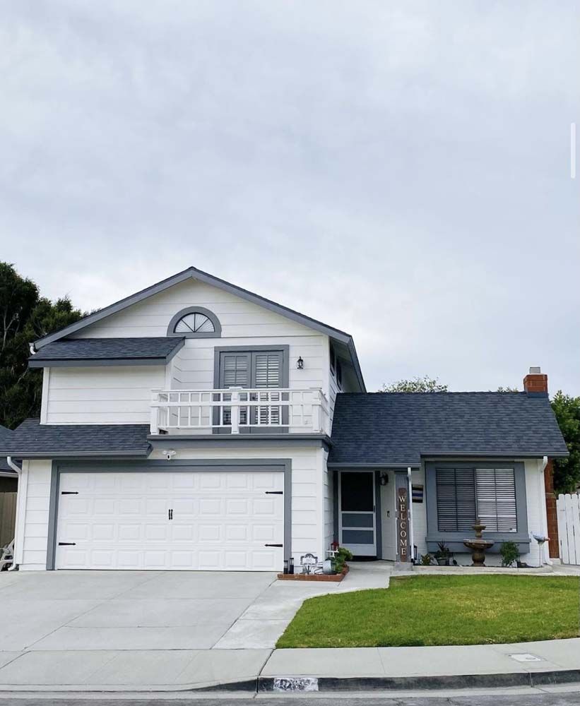 Two-story house with white siding, blue roof, balcony, and attached garage on a gray, overcast day.