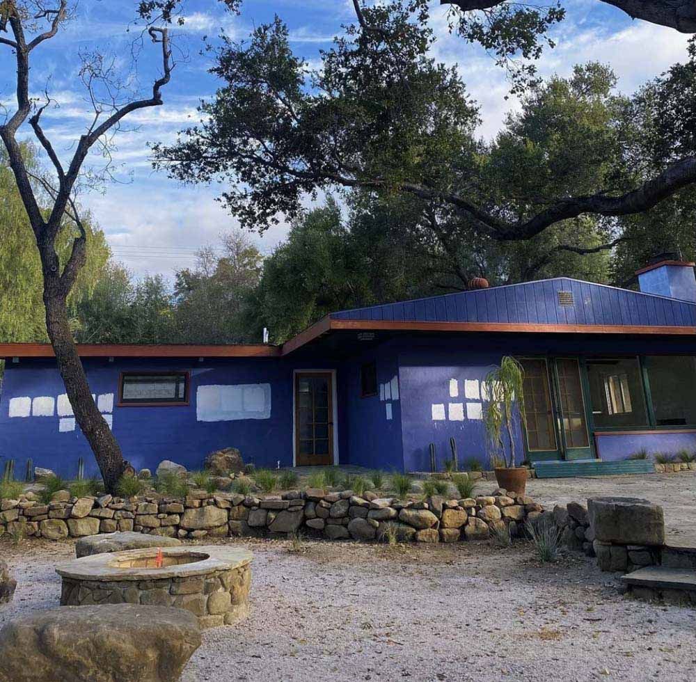 Blue house with a fire pit in the yard, trees in the background.