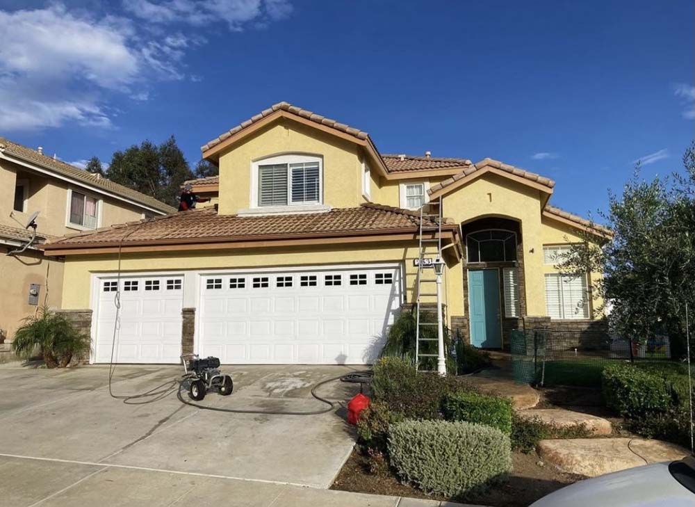 Yellow house with white garage doors, a ladder, and a pressure washer on a driveway.