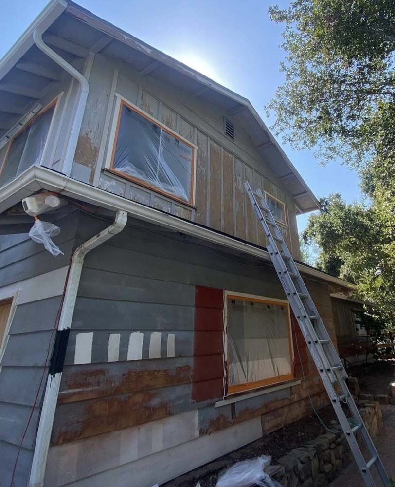 Two-story house with ladder and siding in process of being painted, on a sunny day.