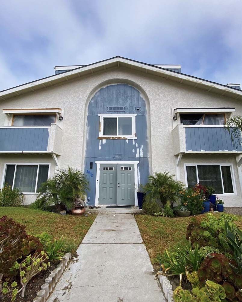 Building exterior with blue and white accents, arched entry. Balconies flank center doors, pathway leads to entrance.
