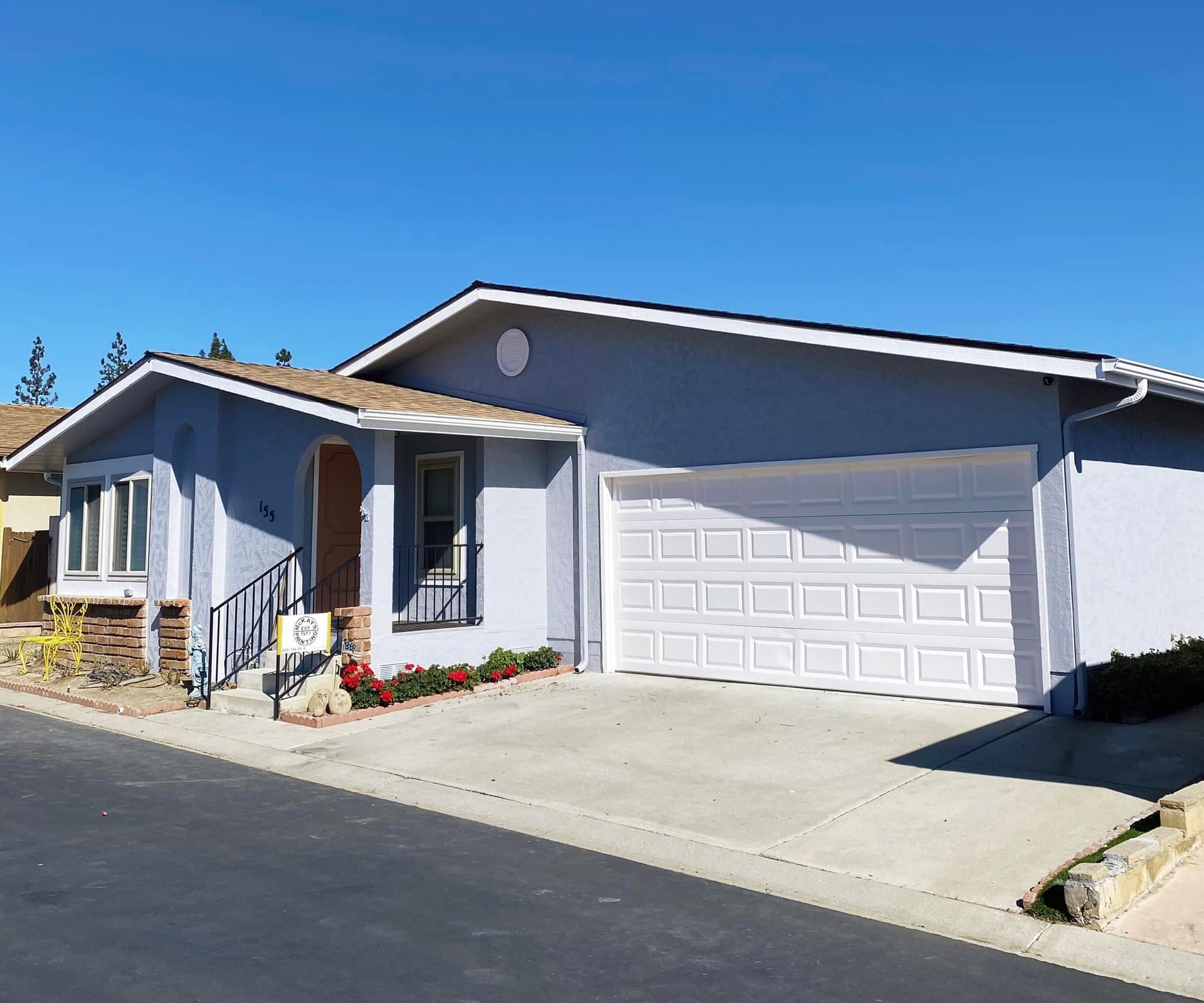 Light blue house with white garage door and concrete driveway on a sunny day.