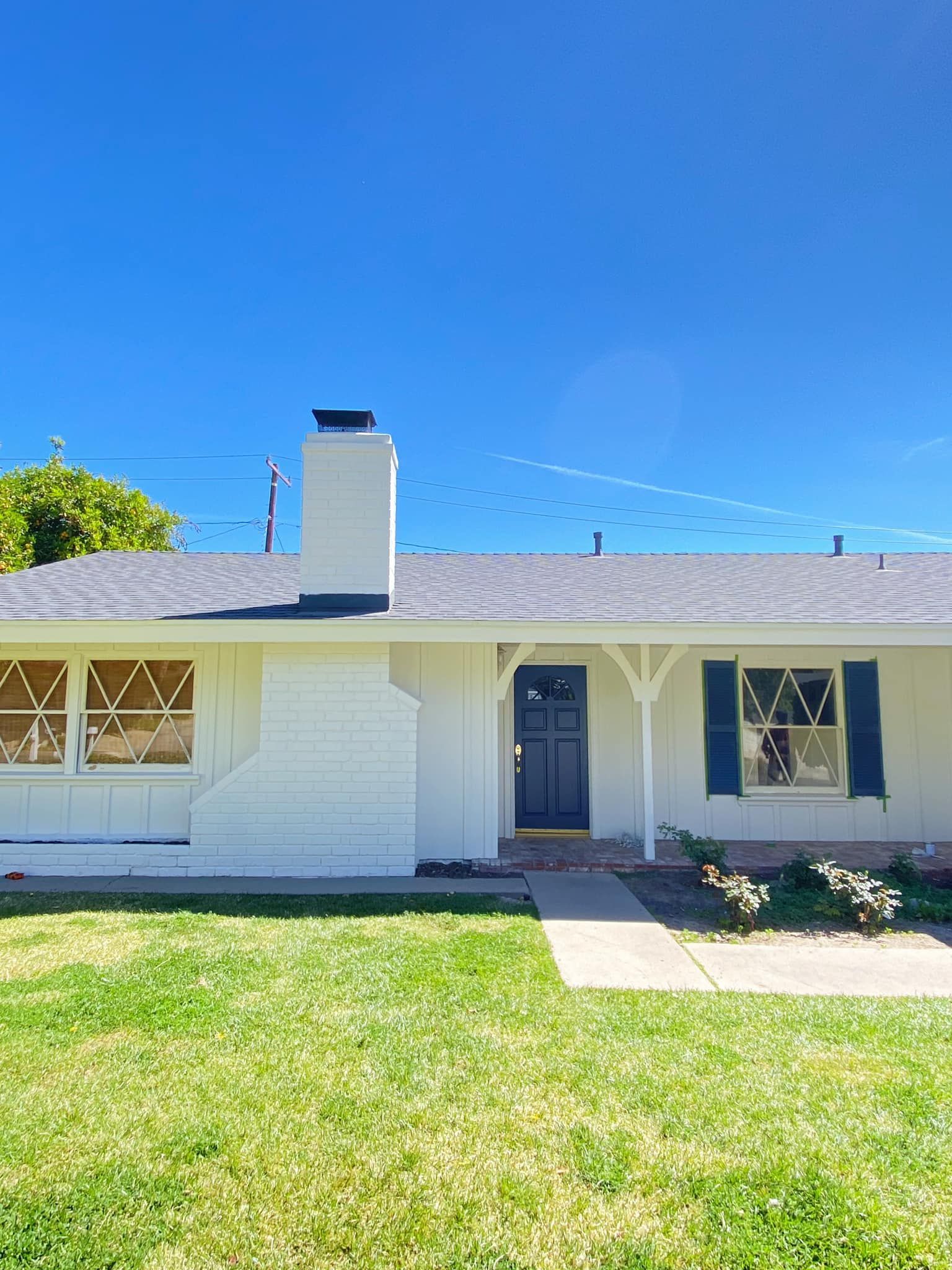 White house with dark blue door and shutters, chimney. Clear blue sky, green grass.