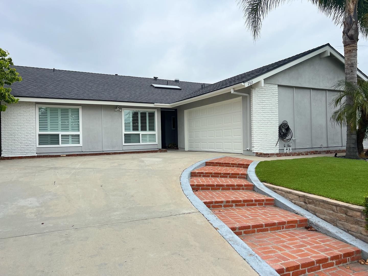 Gray house with a dark roof, white garage door, and brick steps leading to the entrance.