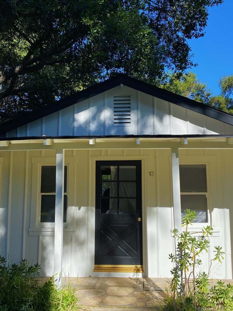 White house with black door, trim, and roof. Two windows flank the door under a porch.
