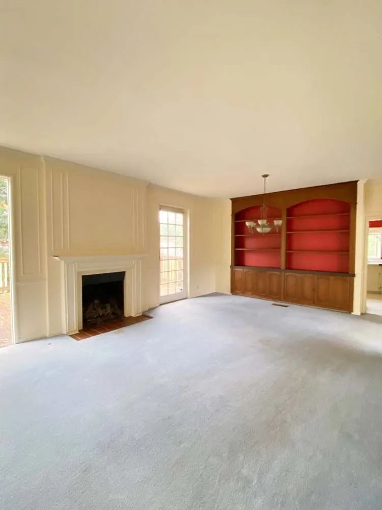 Empty living room with fireplace, built-in shelves, and a red accent wall alcove