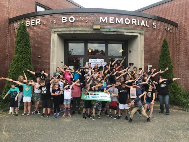 A group of children are posing for a picture in front of a memorial school building.