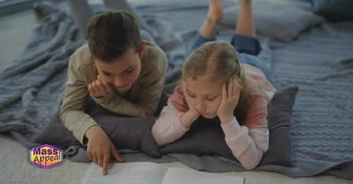 A boy and a girl are laying on the floor reading a book.