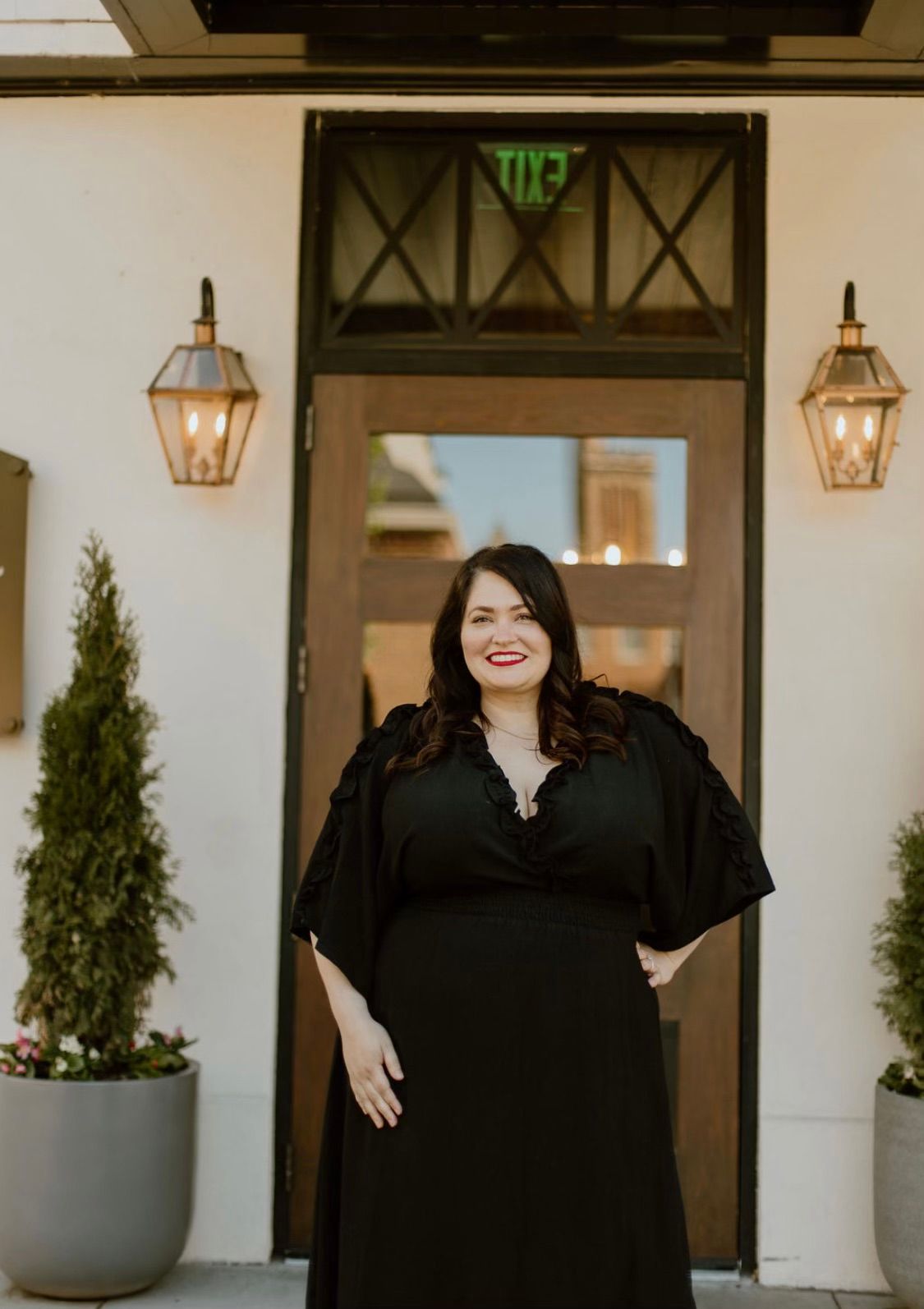A woman in a black dress is standing in front of a door.