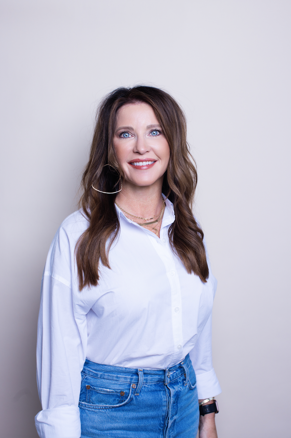A woman wearing a white shirt and blue jeans is smiling for the camera.