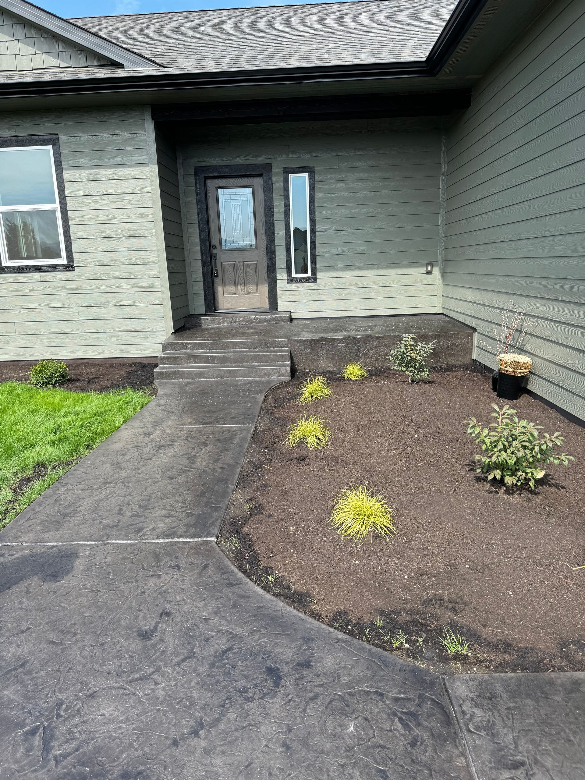 A concrete walkway leading to the front door of a house. Done by Raise the Bar Construction