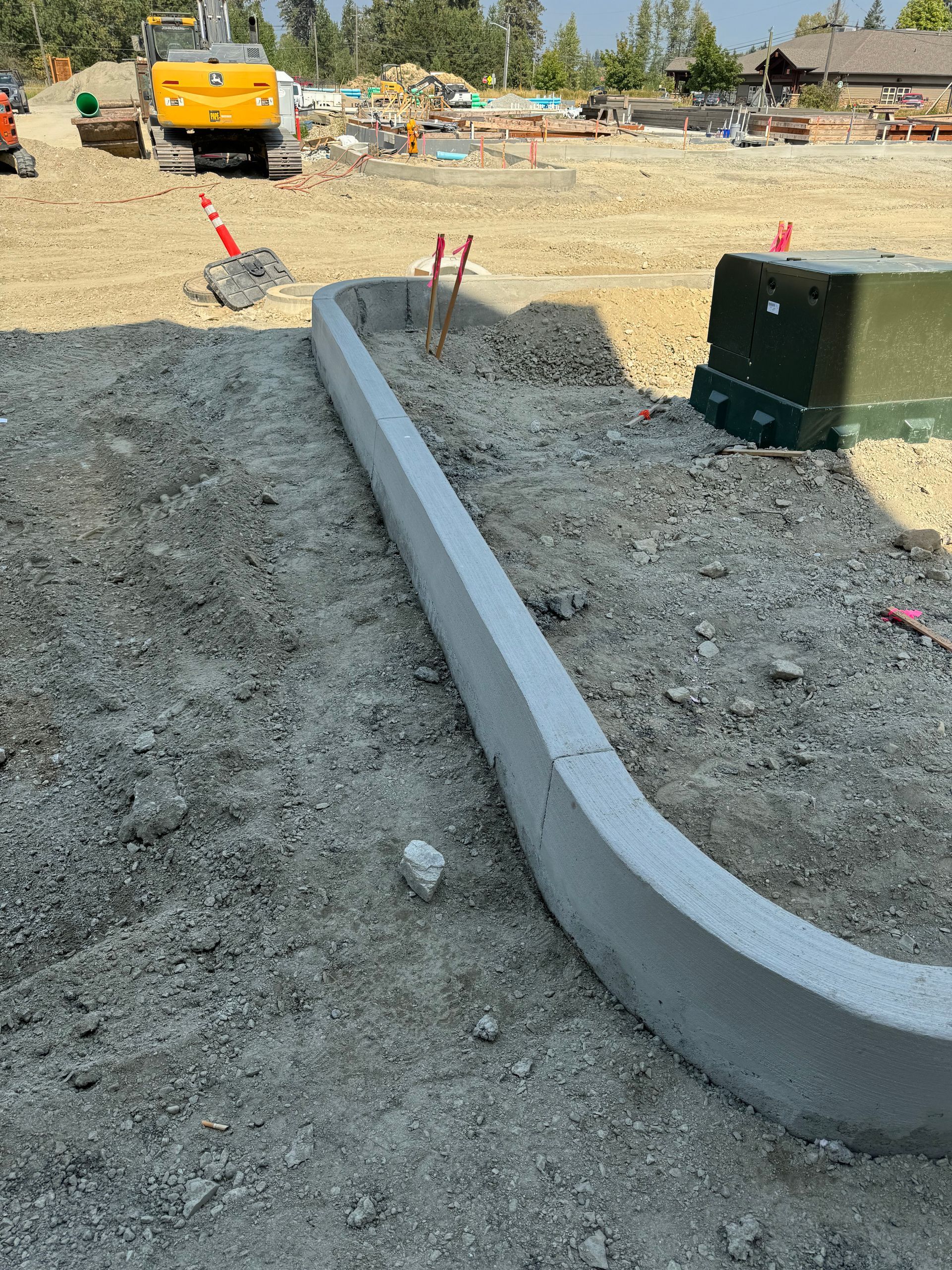 A concrete curb is sitting in the middle of a dirt field. Done by Raise the Bar Construction