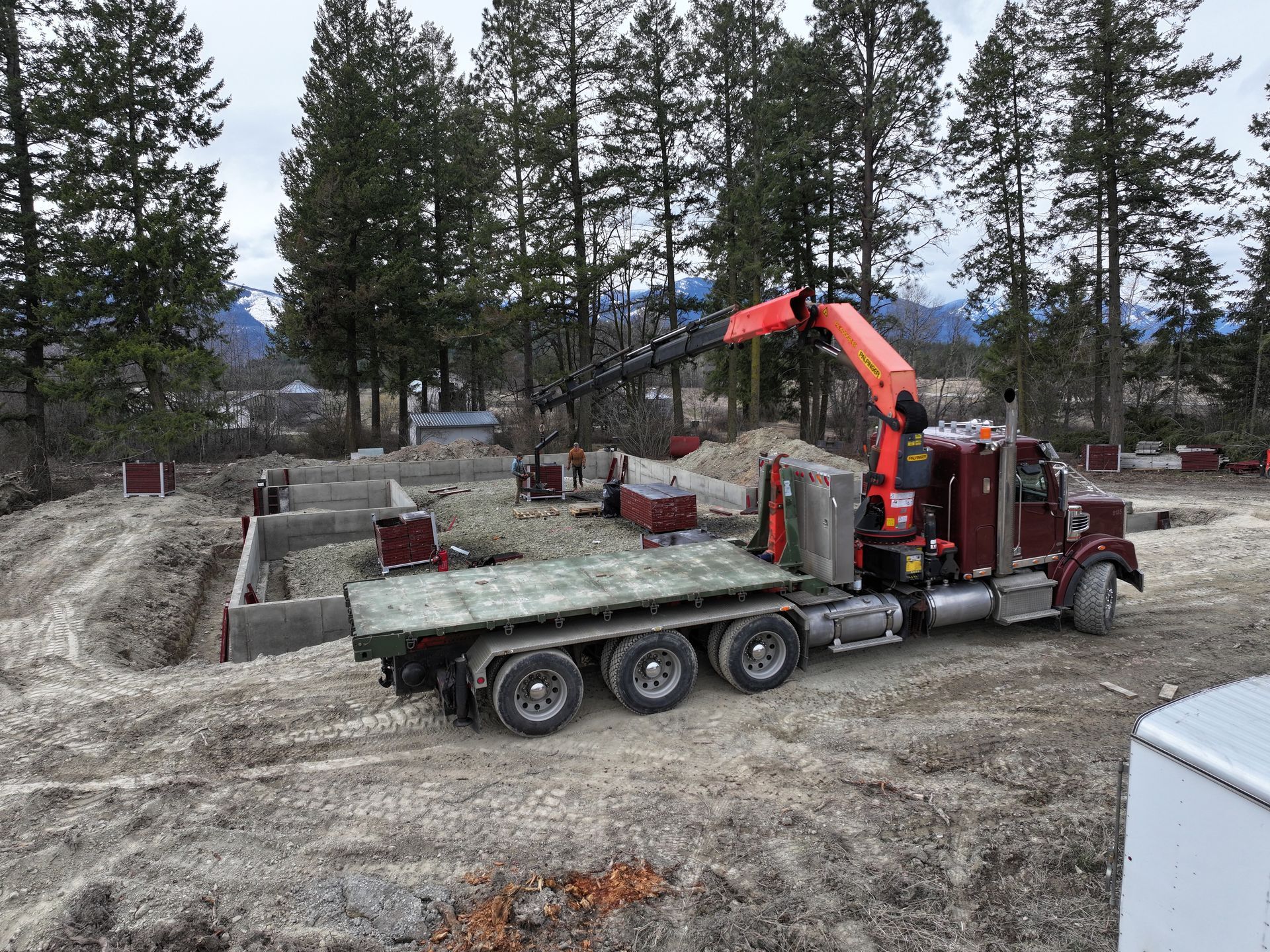 A semi truck with a crane on the back is driving down a dirt road. Project done by Raise the Bar Construction