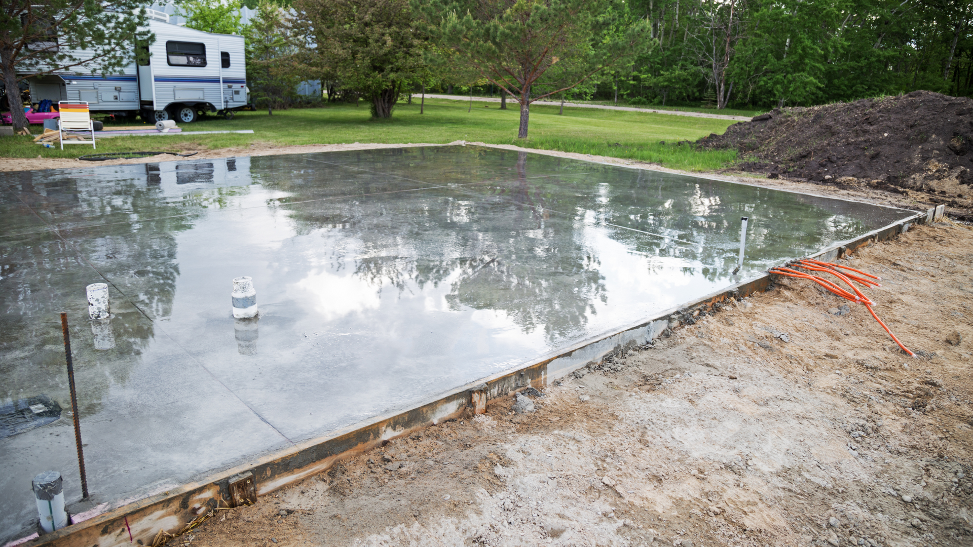 Freshly poured residential concrete slab foundation with plumbing and electrical conduits.