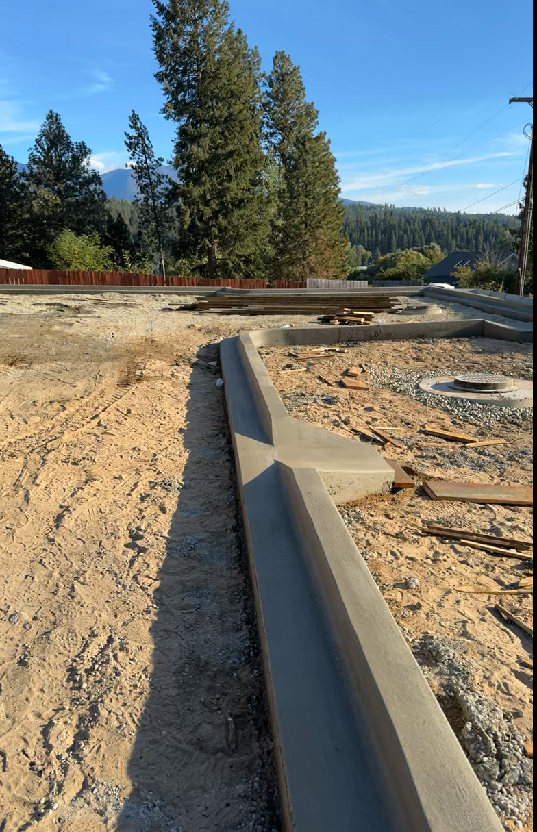 A concrete curb is sitting in the middle of a dirt field. Done by Raise the Bar Construction