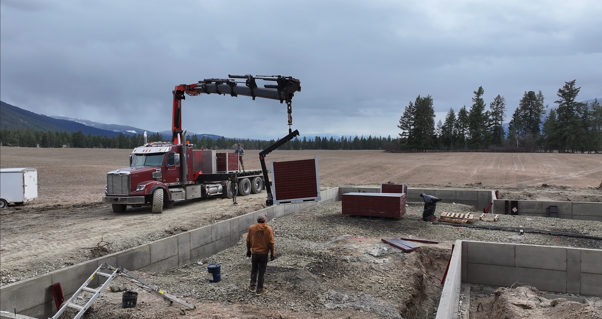 A red truck with a crane attached to it is parked in a dirt field. Done by Raise the Bar Construction
