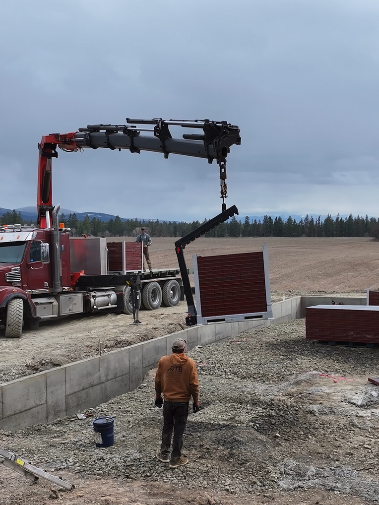 A man walking in front of a red truck with a crane attached to it. Project done by Raise the Bar Construction