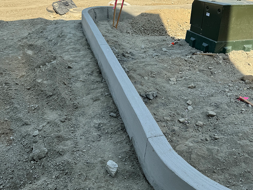 A concrete curb is being built in a dirt field. Done by Raise the Bar Construction