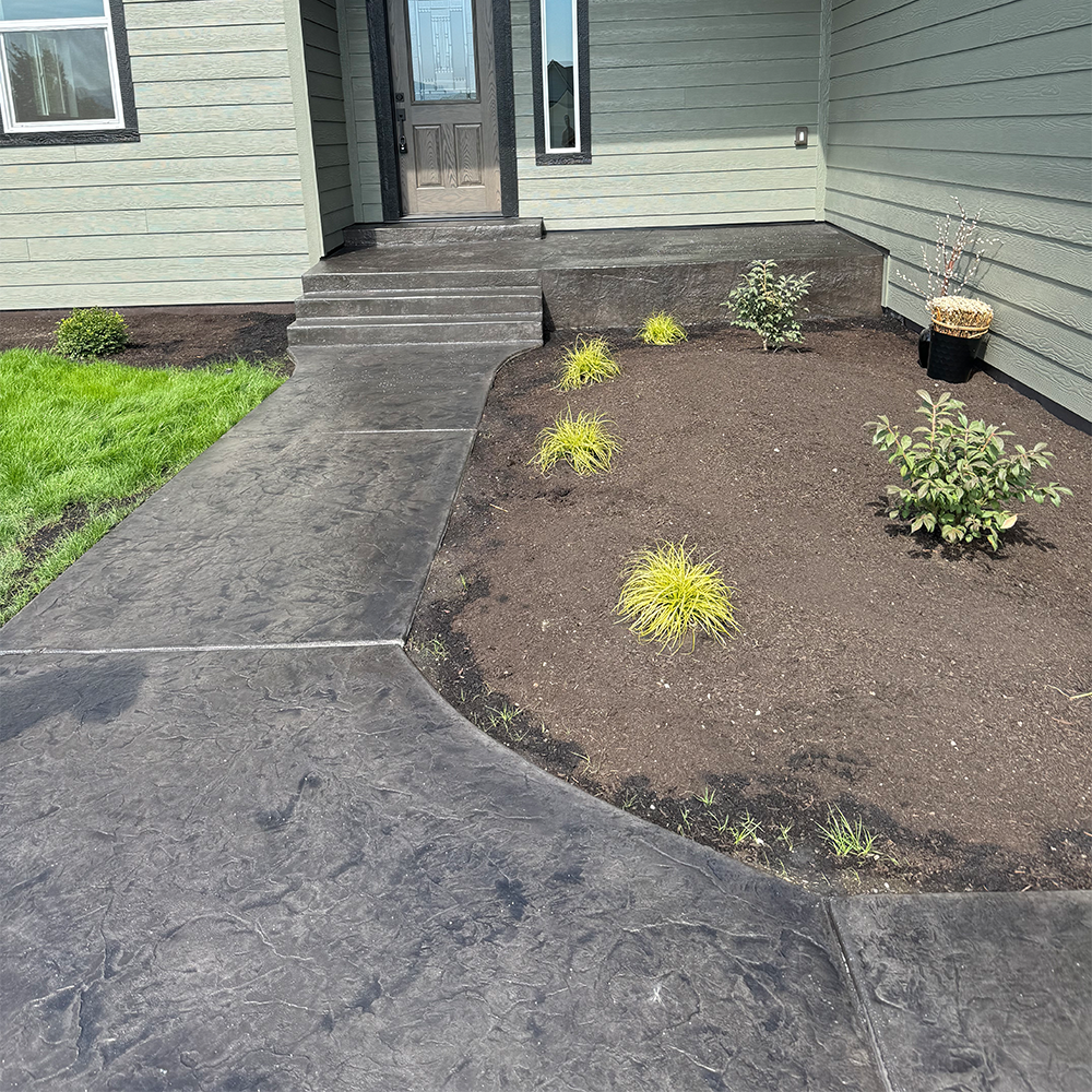 A concrete walkway leading to the front door of a house. Done by Raise the Bar Construction