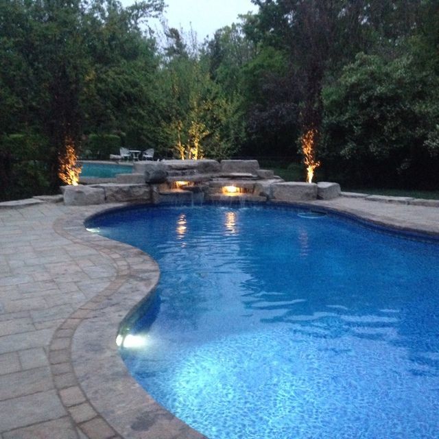 A large swimming pool with a waterfall surrounded by trees