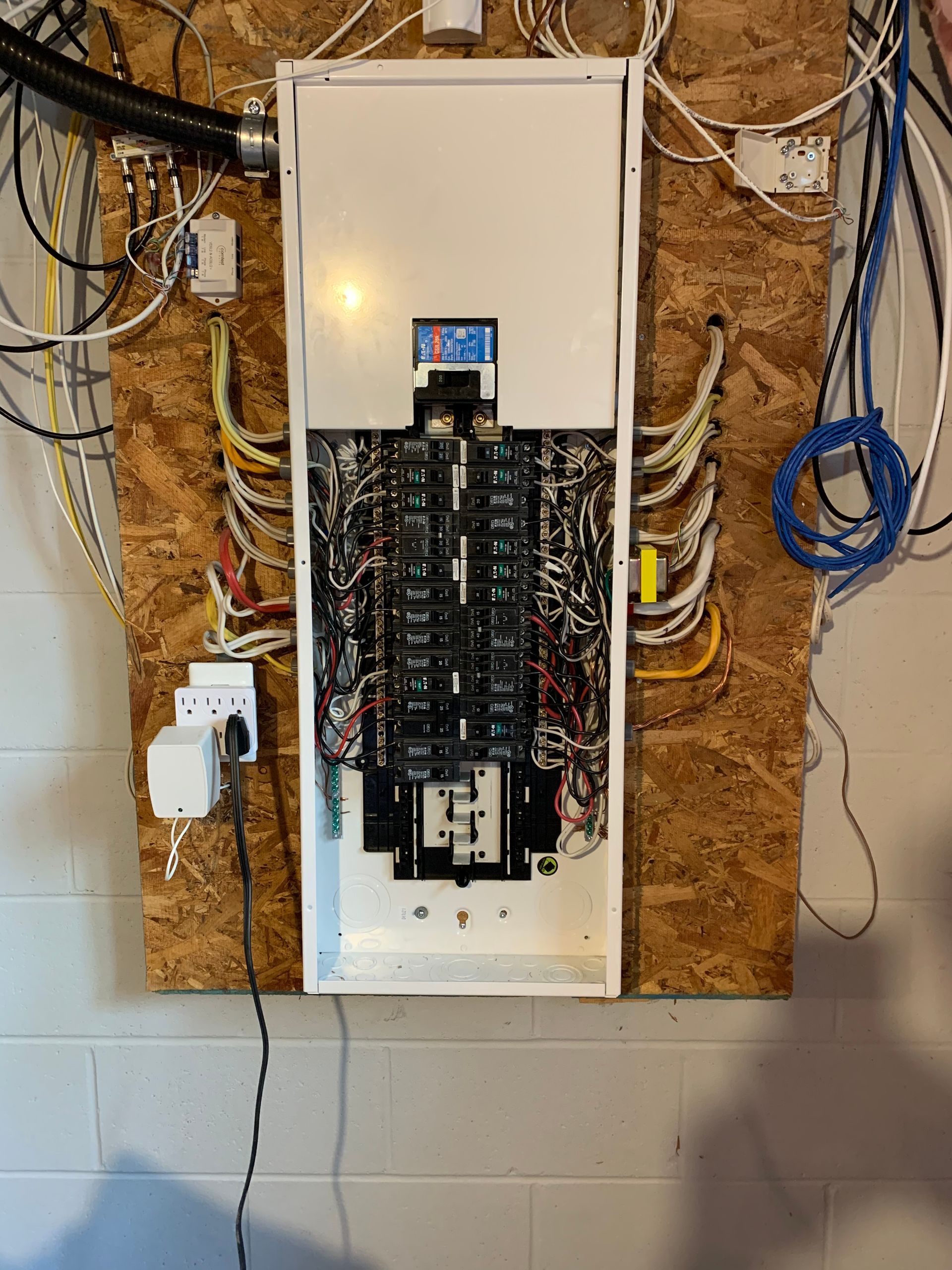 A electrical panel is hanging on a wall with a lot of wires coming out of it.