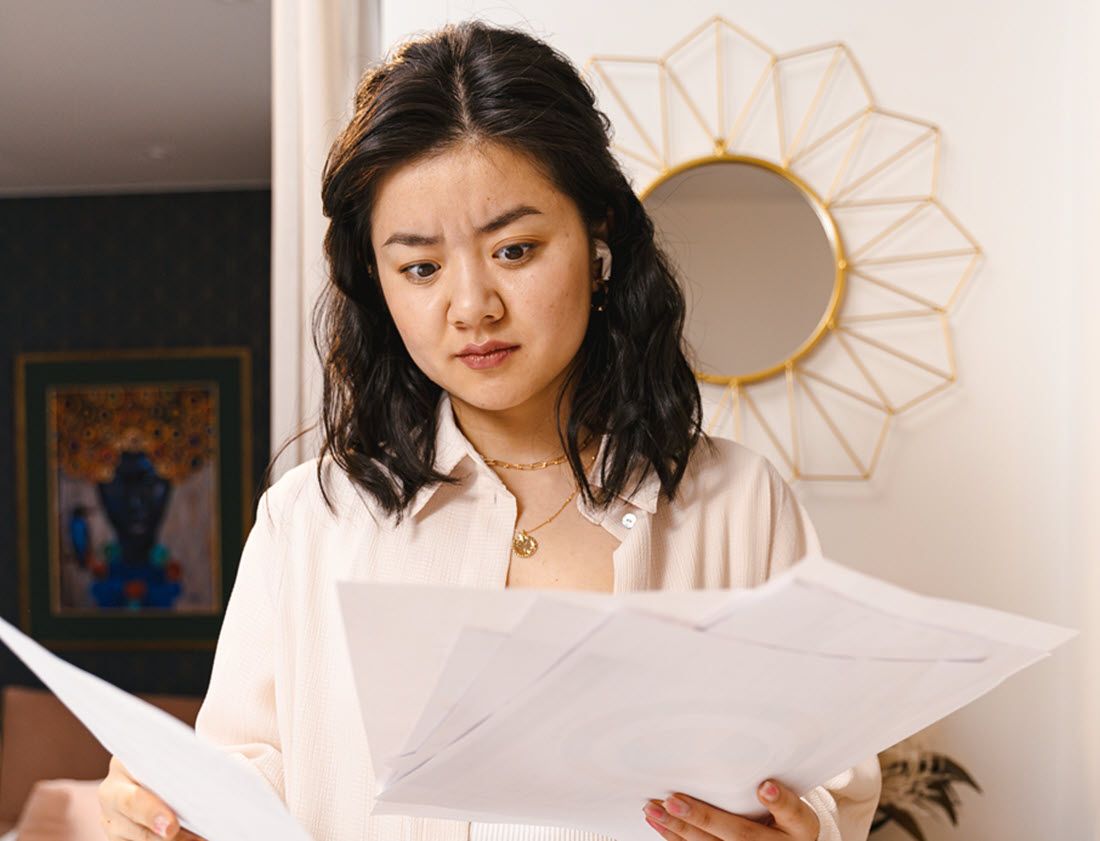 Woman reviewing scattered documents in a room with a decorative wall mirror behind her.