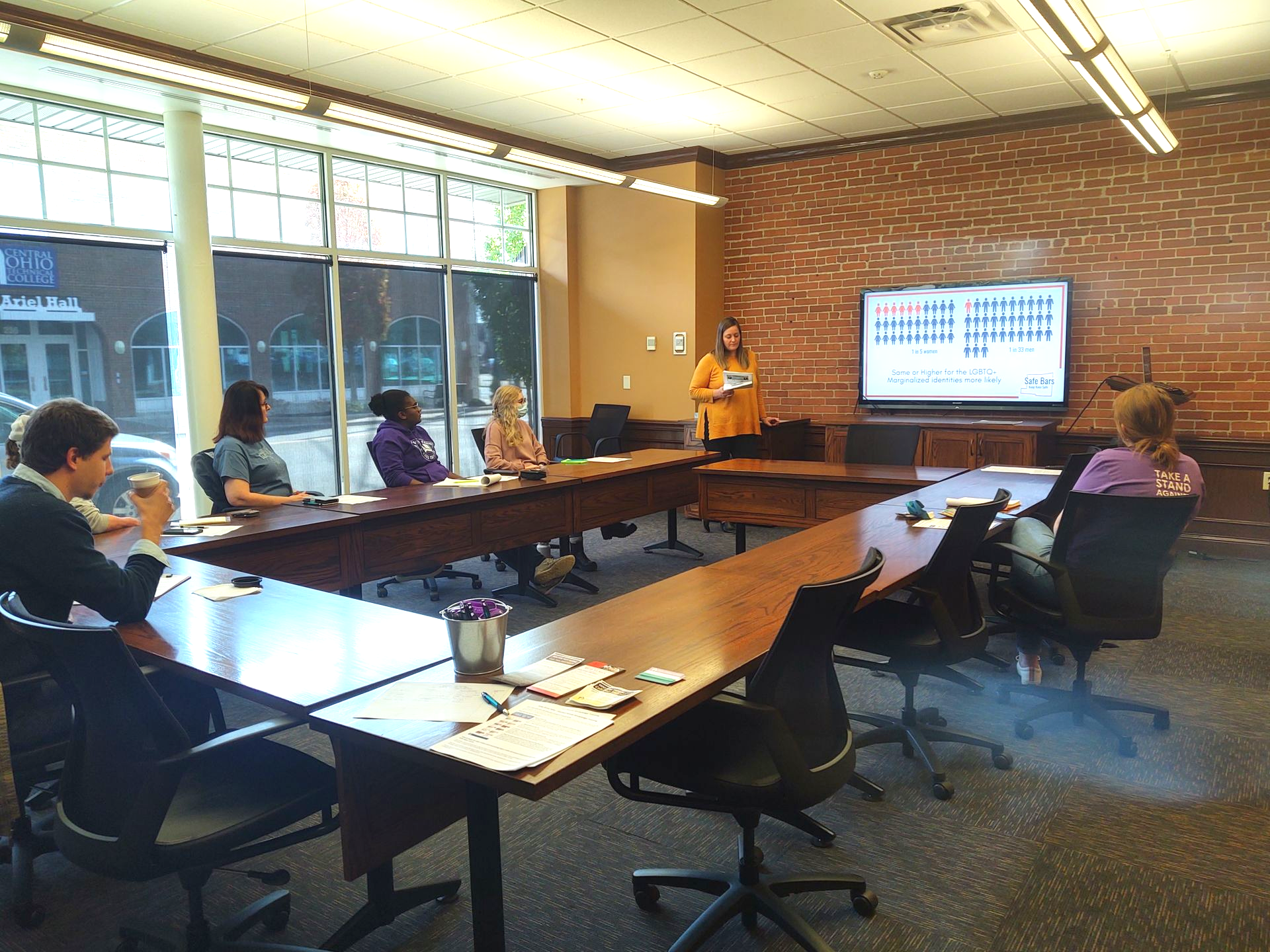 A group of people sitting in white chairs, listening attentively during a seminar or workshop in a bright room.