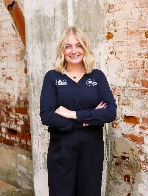 Woman in blue shirt smiles in front of a backdrop with a logo.