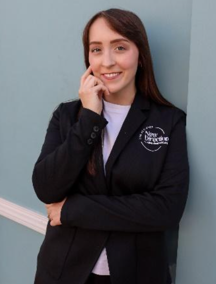 Woman in blue shirt smiles in front of a backdrop with a logo.