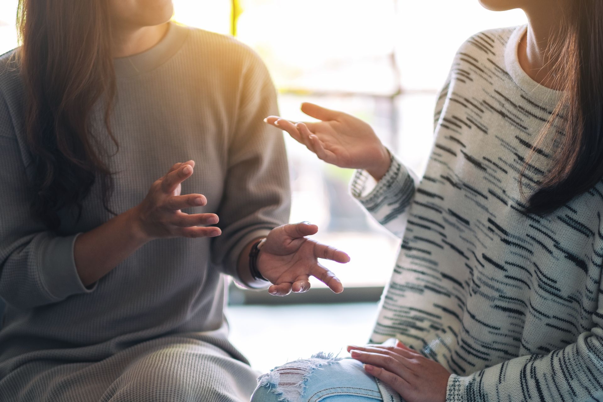 Two people sitting indoors, engaged in a conversation with their hands gesturing.